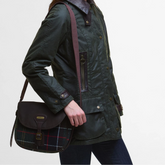 Person wearing a dark green jacket holding a black bag with plaid pattern on a light grey background
